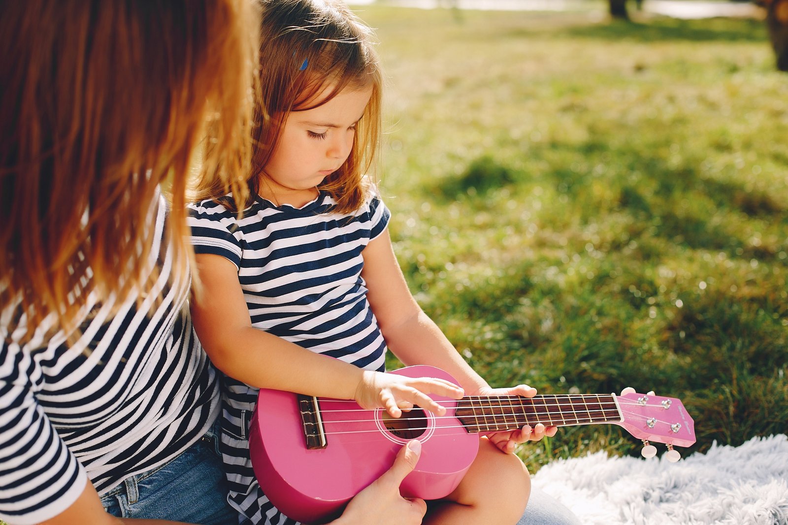 Family sitting in a summer park. Mother in a white t-shirt. Cute little girl with a pink guitar